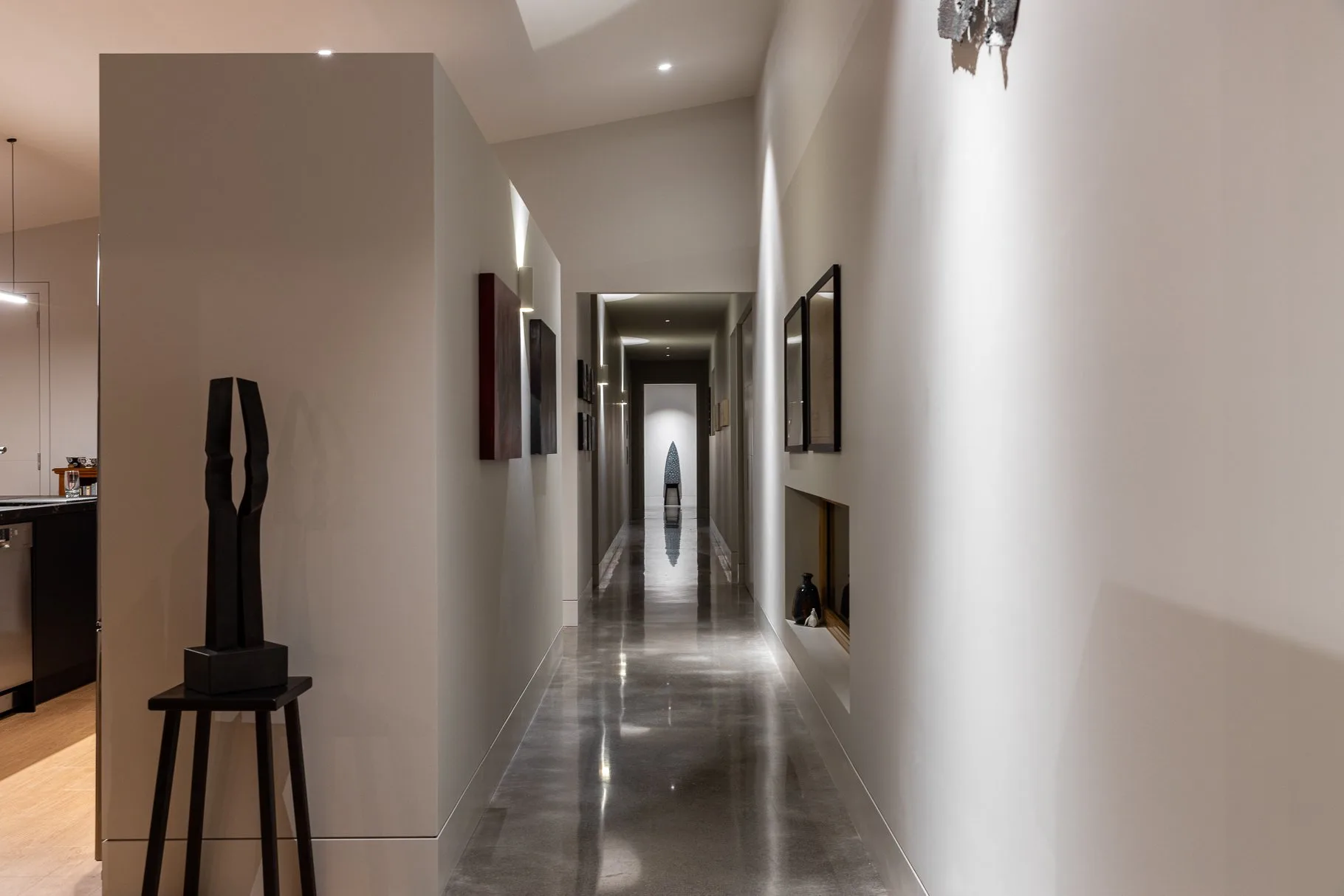 Recessed ceiling lighting and wall sconce illuminating a modern hallway with polished floor.